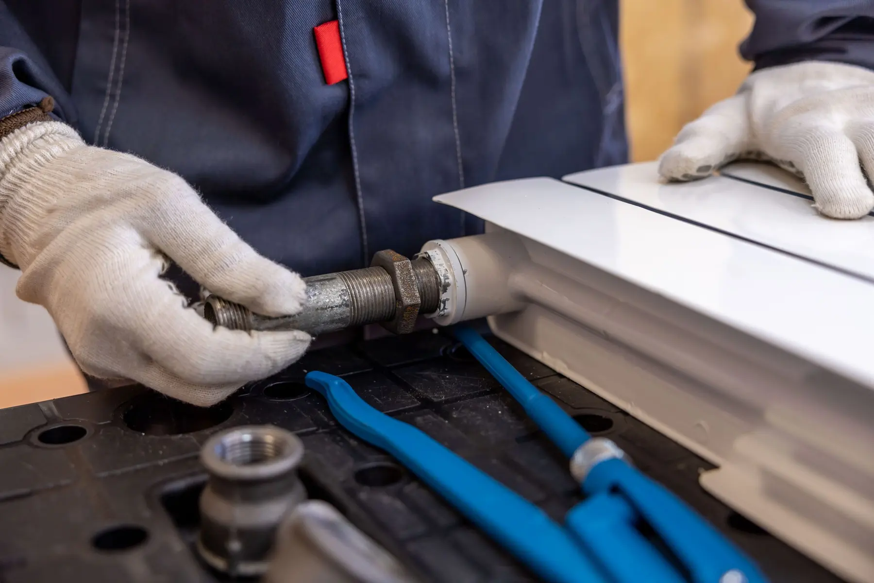 Gloved hands fitting a pipe to a white radiator, spanners beside them (no face)