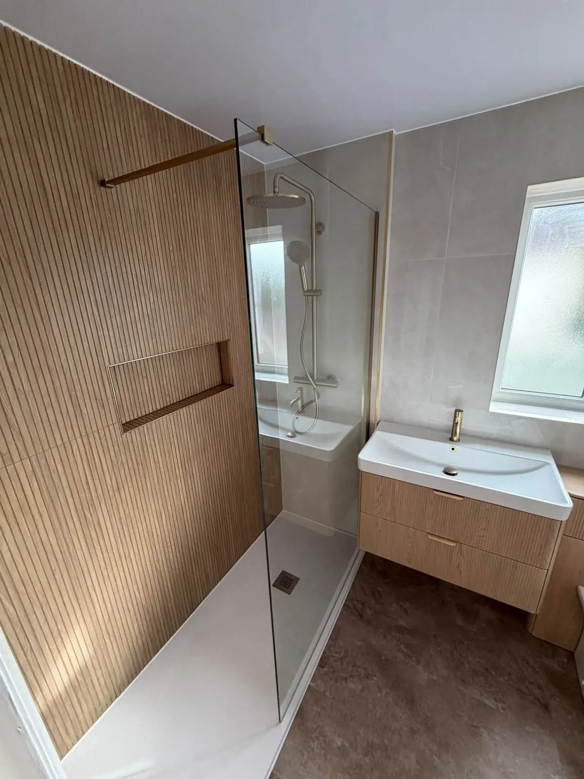 A walk-in shower with a glass screen beside a wood-slat feature wall, and a wall-hung basin unit