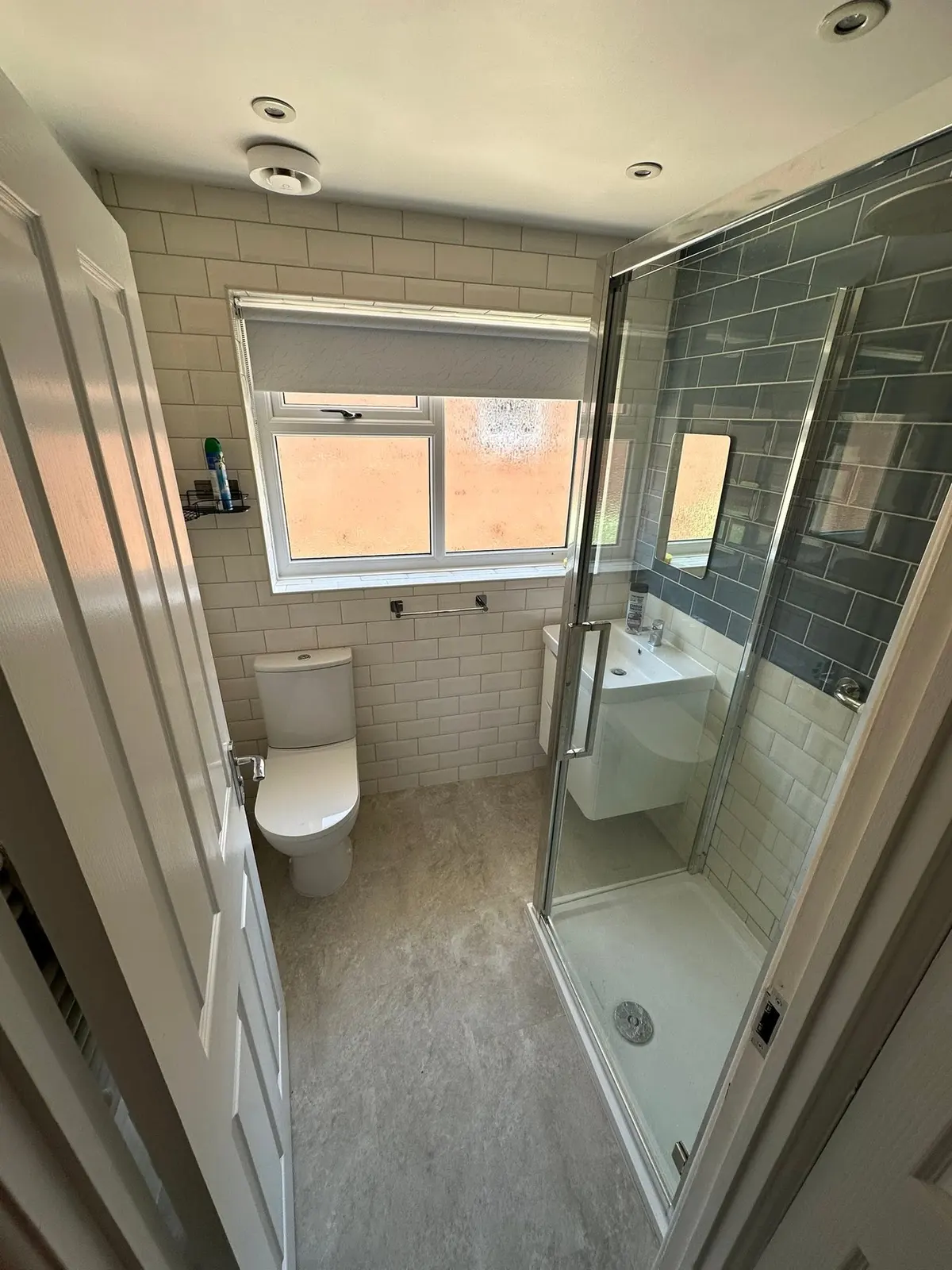 A shower room with a glass shower enclosure, grey and white metro tiles and a toilet
