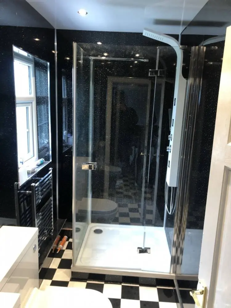 A shower enclosure with black sparkle wall panels and a black and white chequered floor