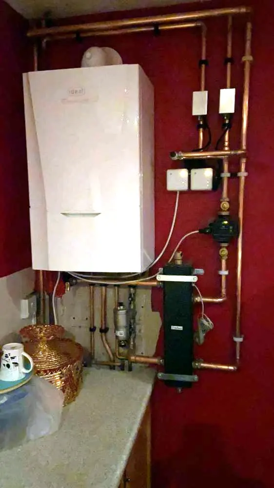A new Ideal boiler on a red wall, with neat copper pipework and its controls beside it